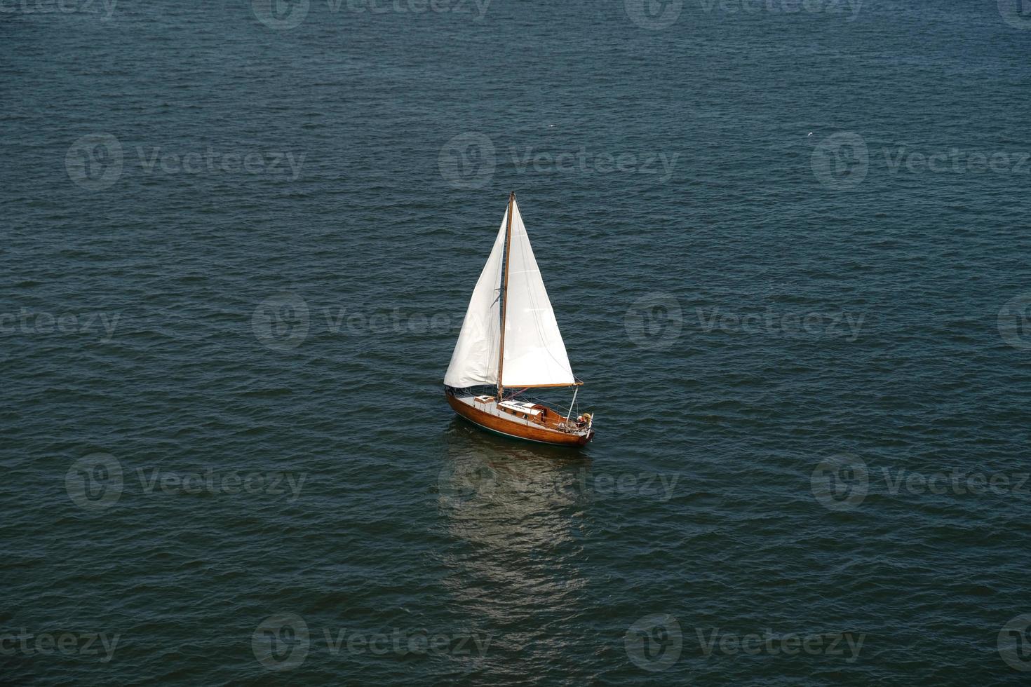 Aerial view of wooden old yacht with sail against backdrop of blue water with waves and ripples. Lonely white sail is sailing. Perfect content for posters or advertising banners, creative projects. photo