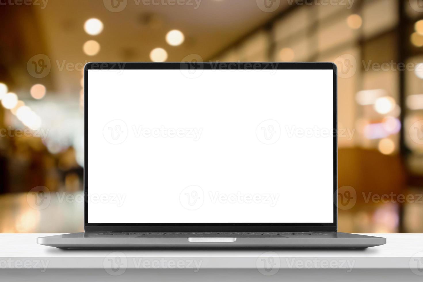 Laptop with blank screen on marble table with cafe coffee shop blur background photo