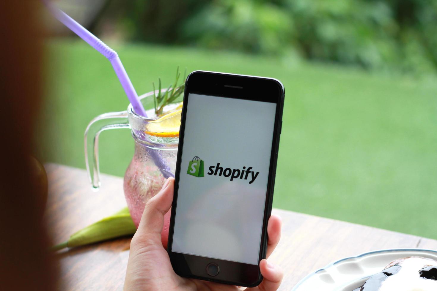 chiang mai, tailandia - 11 de julio de 2020 - una mujer sostiene un teléfono móvil iphone 7 plus con aplicación shopify en la pantalla en una panadería y cafetería. Shopify es una plataforma de comercio electrónico para tiendas en línea. foto