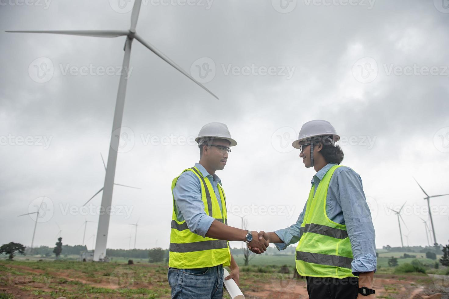 Two engineers working and holding the report at wind turbine farm Power Generator Station on mountain,Thailand people,Technician man and woman discuss about work photo