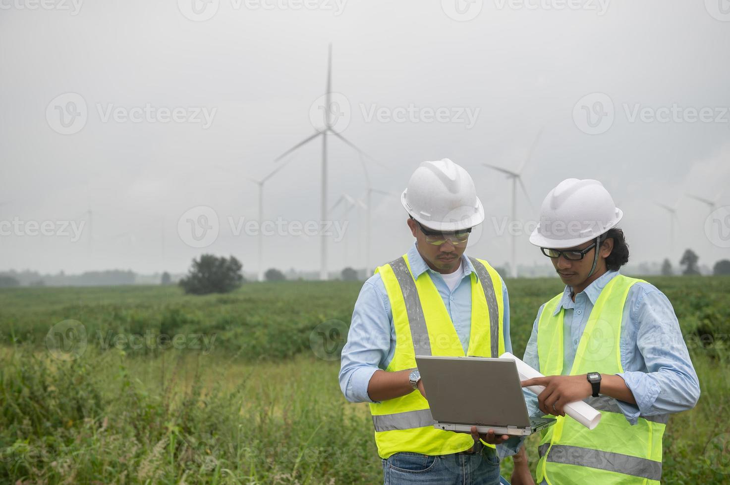 Two engineers working and holding the report at wind turbine farm Power Generator Station on mountain,Thailand people,Technician man and woman discuss about work photo