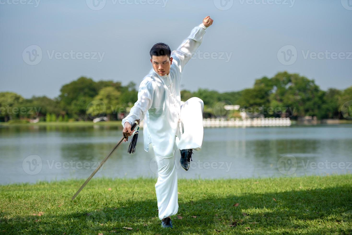 joven practicando la espada tradicional de tai chi, tai ji en el parque para el concepto saludable y tradicional de artes marciales chinas sobre fondo natural. foto