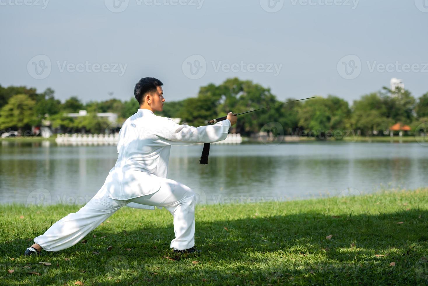 joven practicando la espada tradicional de tai chi, tai ji en el parque para el concepto saludable y tradicional de artes marciales chinas sobre fondo natural. foto