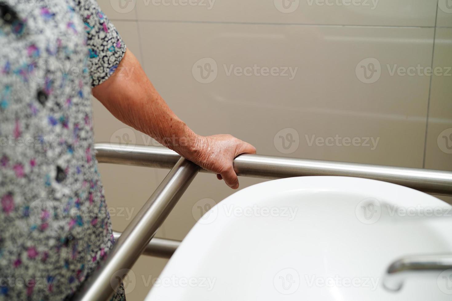 una paciente asiática usa un riel de soporte para el inodoro en el baño, barra de seguridad para pasamanos, seguridad en el hospital de enfermería. foto