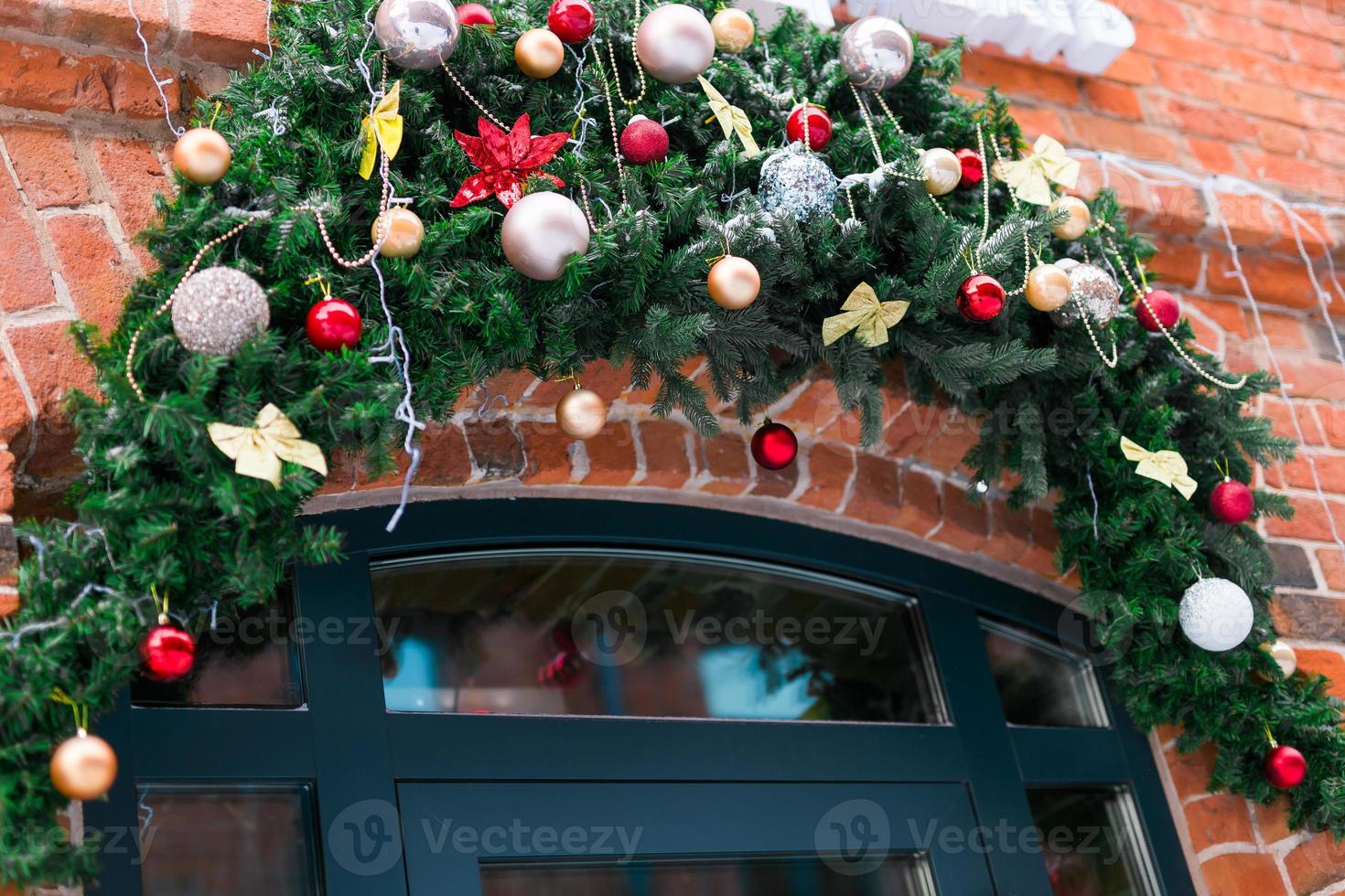 Stylish christmas fir branches with baubles and sparkling garland on front of door at holiday market or restaurant in city street. Winter christmas street decor photo