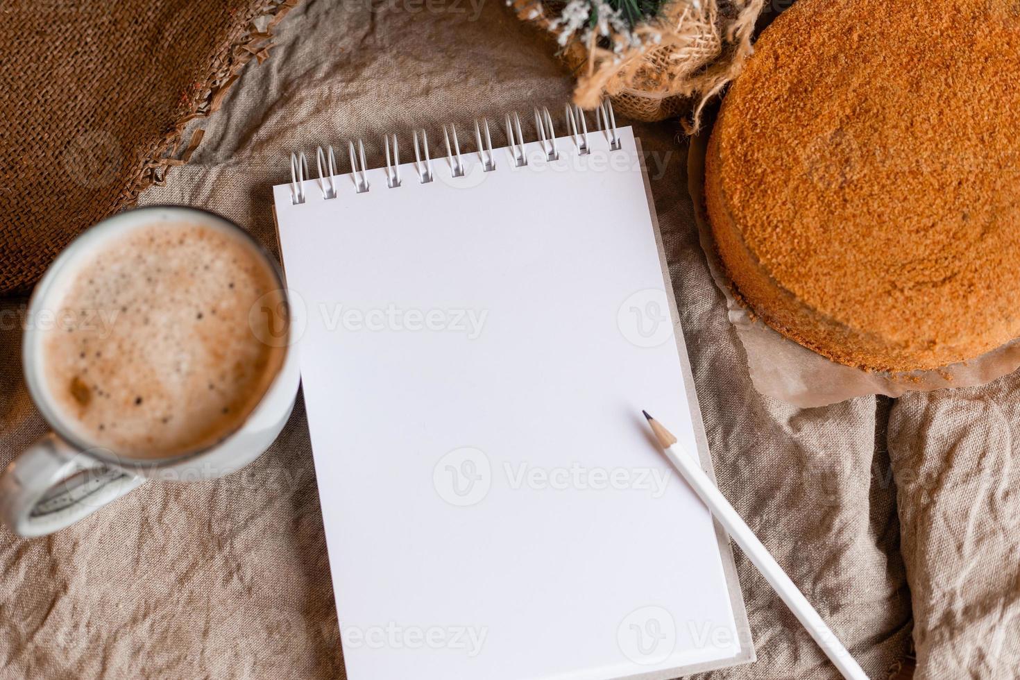 a notebook with empty pages on a wooden table with coffee and homemade honey cake. A notebook for recipes, cooking at home. Homemade cakes, space for text photo