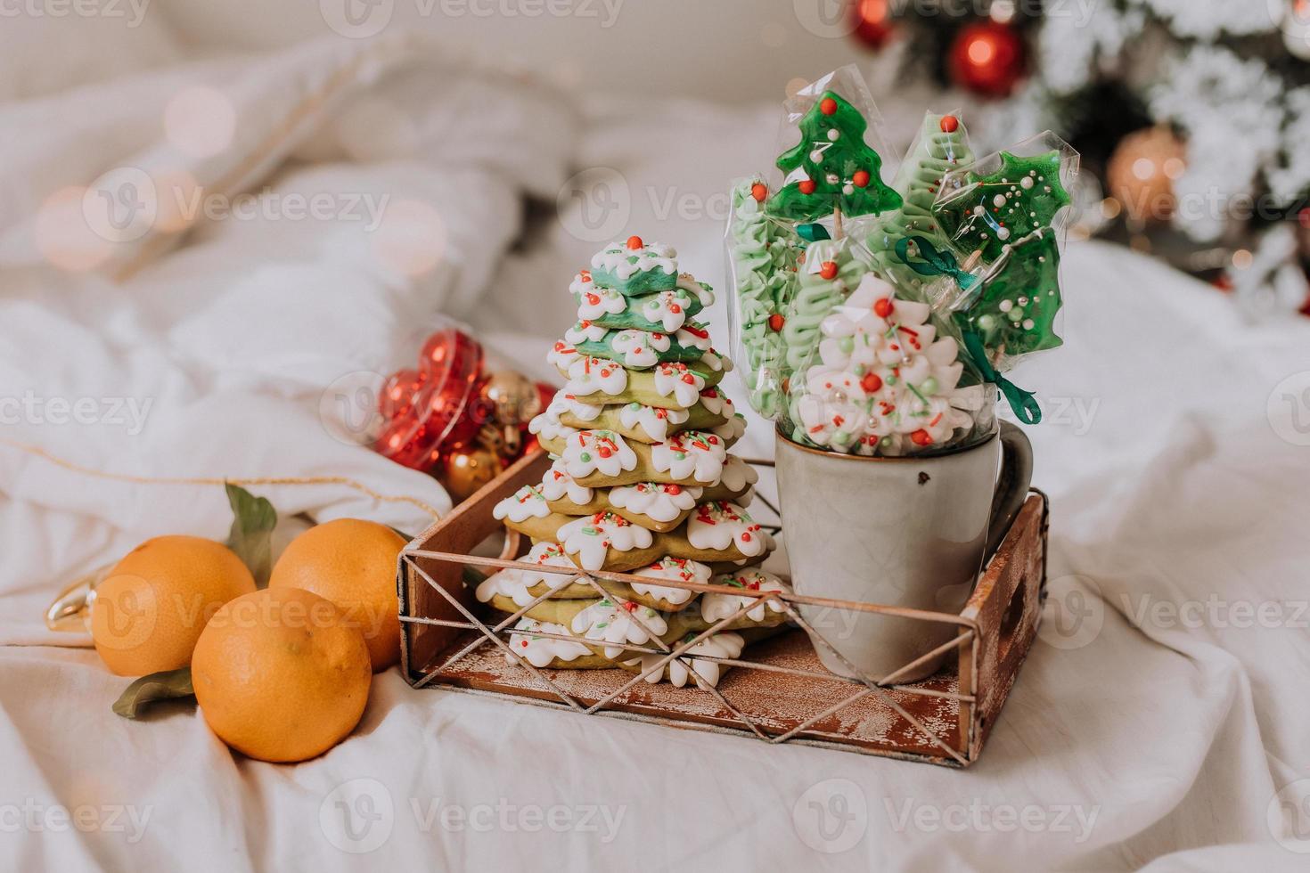 Christmas sweets, gingerbread painted with icing, lollipops and meringues in the shape of Christmas trees and tangerines on a beautiful tray. homemade cakes. delicious food for the winter holidays photo