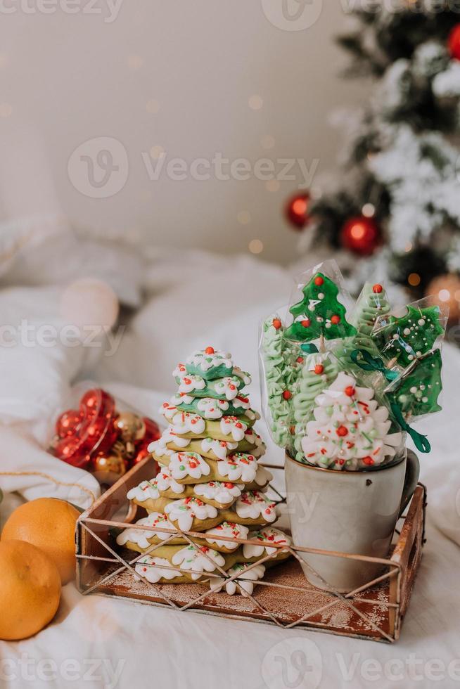 dulces navideños, pan de jengibre pintado con glaseado, piruletas y merengues en forma de árboles de navidad y mandarinas en una bonita bandeja. tortas caseras deliciosa comida para las vacaciones de invierno foto