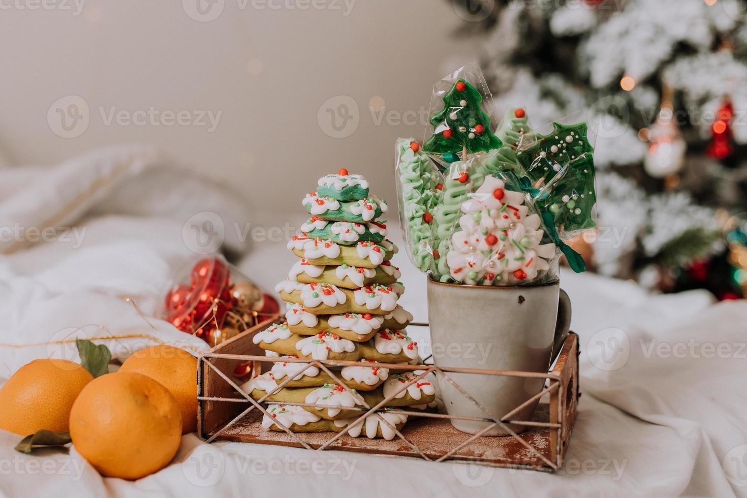 Christmas sweets, gingerbread painted with icing, lollipops and meringues in the shape of Christmas trees and tangerines on a beautiful tray. homemade cakes. delicious food for the winter holidays photo