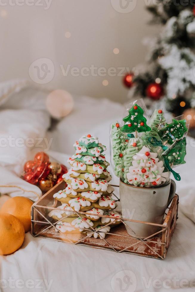 dulces navideños, pan de jengibre pintado con glaseado, piruletas y merengues en forma de árboles de navidad y mandarinas en una bonita bandeja. tortas caseras deliciosa comida para las vacaciones de invierno foto