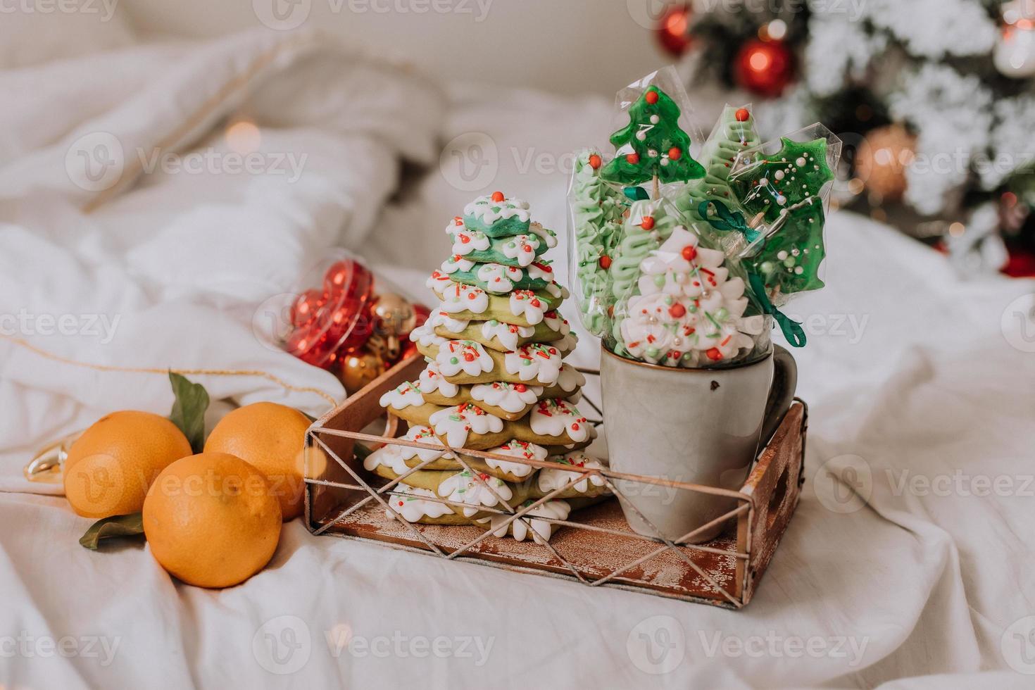 dulces navideños, pan de jengibre pintado con glaseado, piruletas y merengues en forma de árboles de navidad y mandarinas en una bonita bandeja. tortas caseras deliciosa comida para las vacaciones de invierno foto