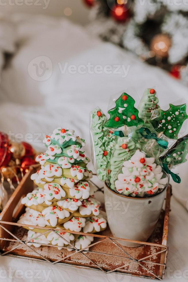 Christmas sweets, gingerbread painted with icing, lollipops and meringues in the shape of Christmas trees and tangerines on a beautiful tray. homemade cakes. delicious food for the winter holidays photo