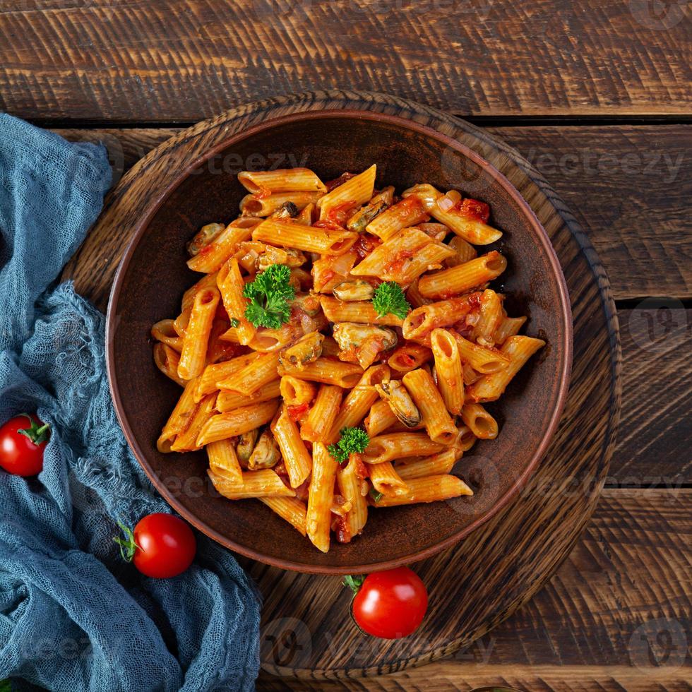 Pasta penne in marinara sauce with mussels, onion and parsley. Classic Italian pasta penne. Top view photo