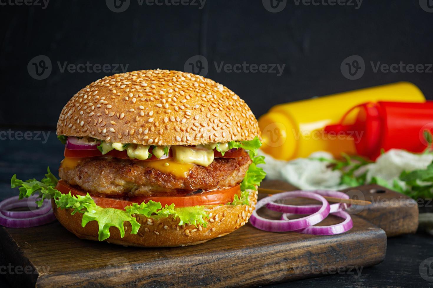 hamburguesa clásica casera con chuleta de ternera, queso, lechuga y tomate sobre fondo oscuro foto