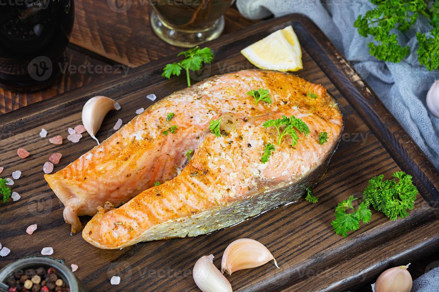 Baked salmon steak with herbs on wooden cutting board. Grilled salmon with salt and pepper photo