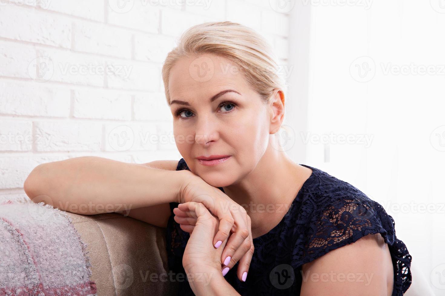 Beautiful middle-aged woman looking in camera in living room. photo