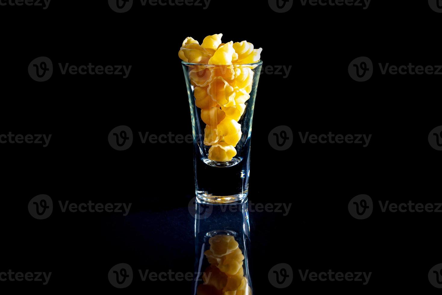 raw pasta in glass jar, wine glass. in bucket. raw pasta on black background. front view raw pasta, dropped from hand, place for text, yellow long spaghetti straws, photo