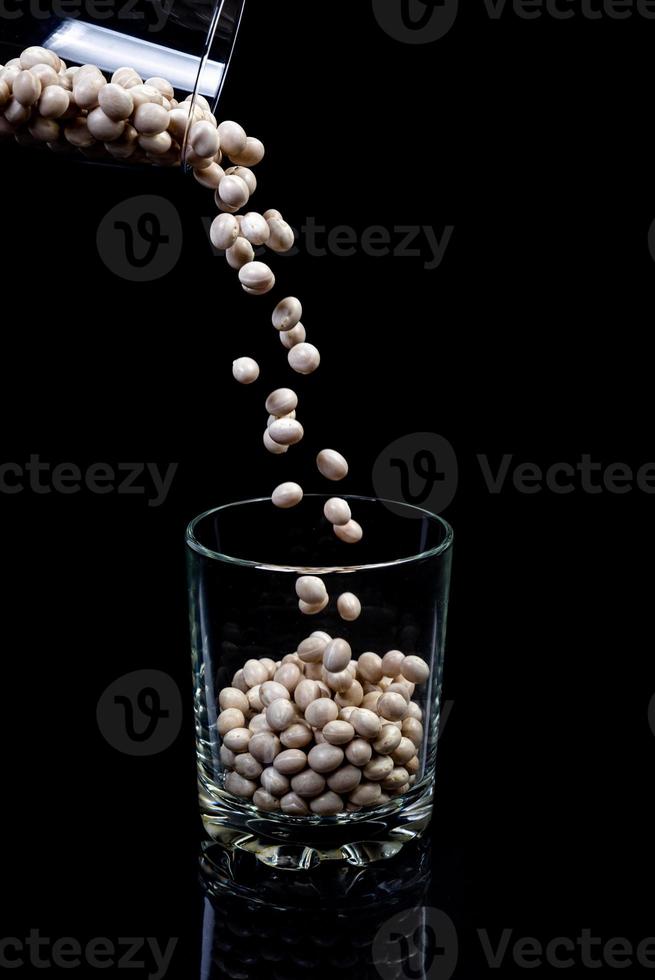 raw white beans in glass jar, wine glass. in bucket. raw white beans on black background. front view raw white beans, dropped from hand, isolated photo