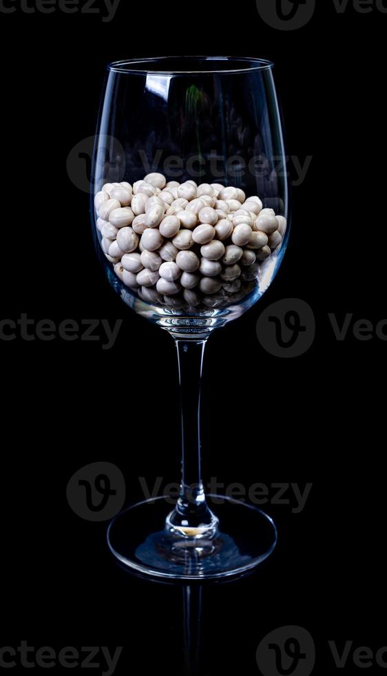 judías blancas crudas en tarro de cristal, copa de vino. en cubo. judías blancas crudas sobre fondo negro. frijoles blancos crudos de vista frontal, caídos de la mano, aislados foto