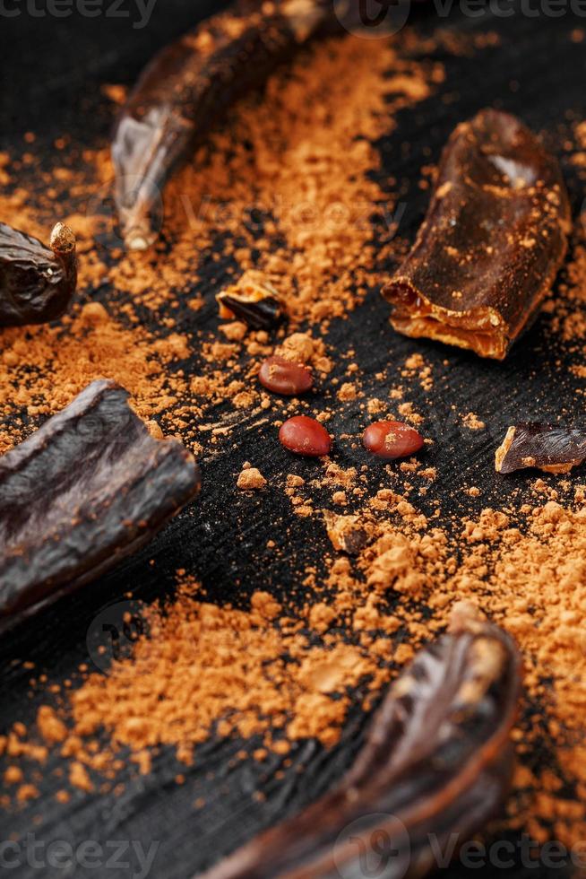 Carob carob fruit with powder on black background. Blast the Sweet powder from the pulp of the pods. photo