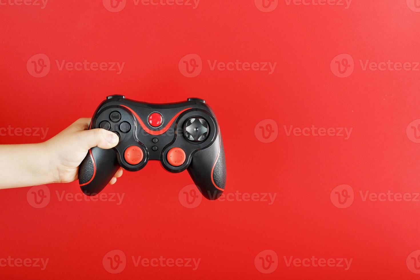 A child's hand holds a gamepad on a red background. Free space, minimalistic creative concept of the Younger generation of gamers. photo