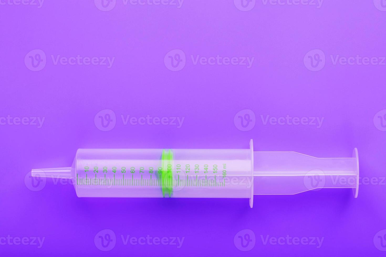 Green medical syringe on crazy lilac background. The concept of minimalism and free space. photo