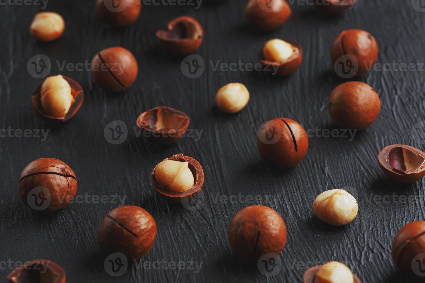 Purified and shell repeats macadamia nuts on black textural stone background. Healthy eating concept. Low contrast photo