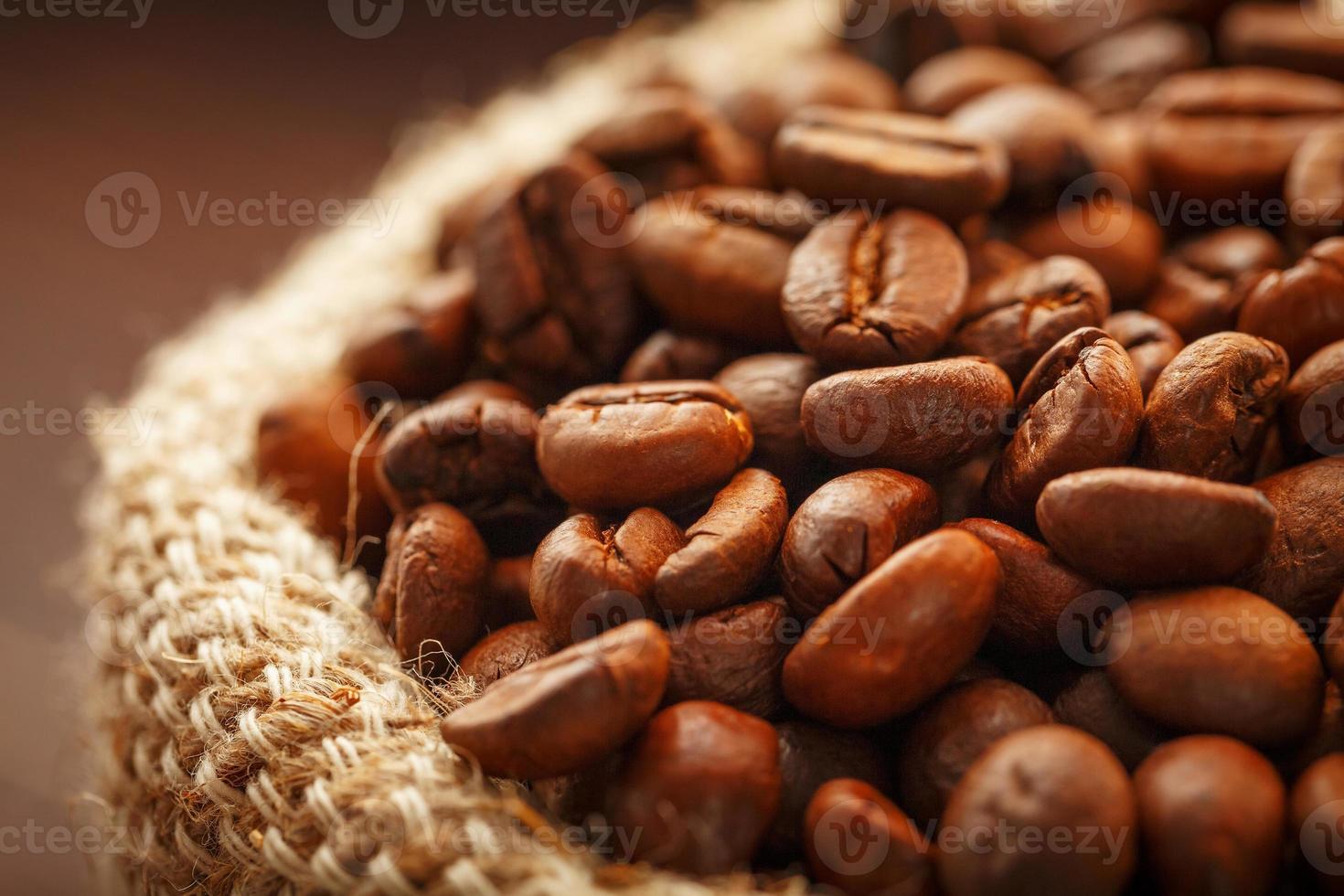 Coffee beans closeup in burlap bag on wooden background. photo