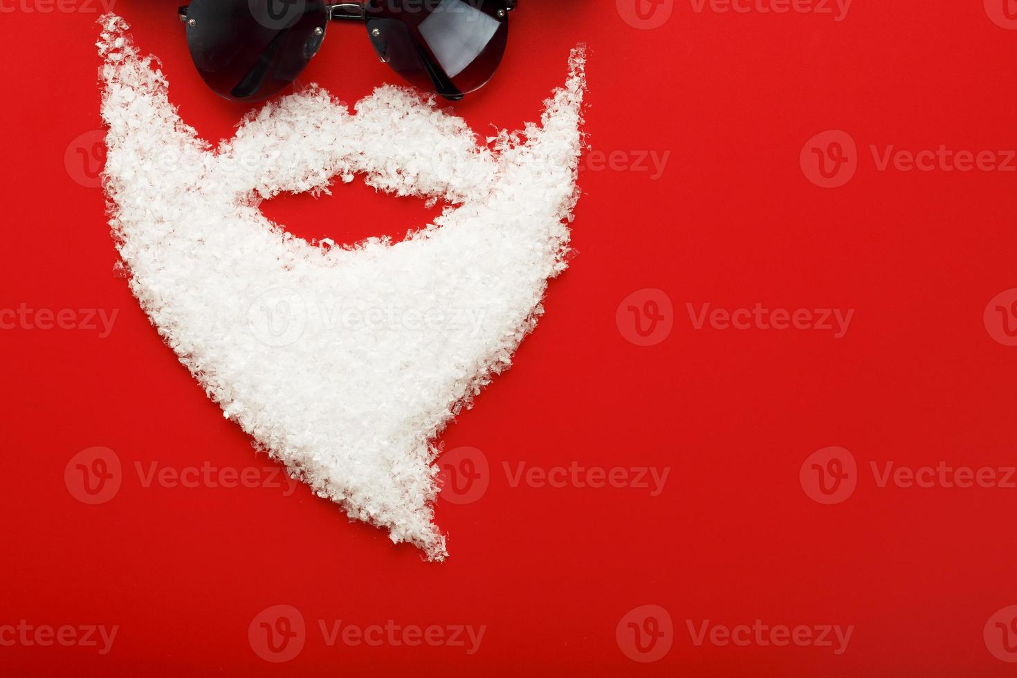 Santa Claus with black glasses and beard made of snow on red background. photo