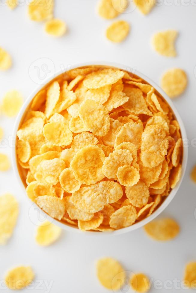 White cup with golden corn flakes, isolated on white background. Hopya crumbled around the cup. View from above photo