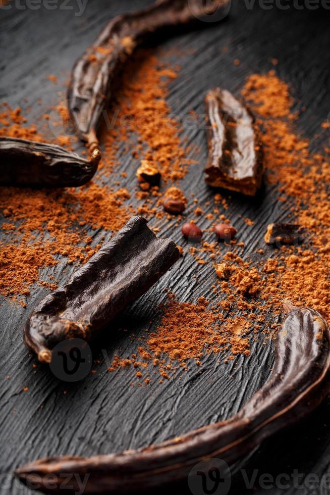 Carob carob fruit with powder on black background. Blast the Sweet powder from the pulp of the pods. photo