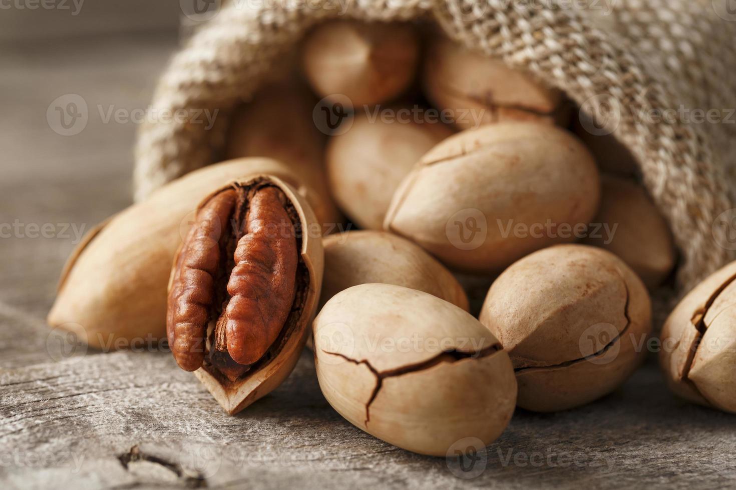 Pecans spill out of a bag on a wooden table, close-up. Peeled, in a shell. photo