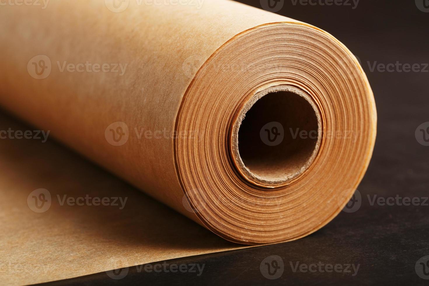 A roll of unfolded brown parchment paper, for baking food in on a dark background, top view. photo