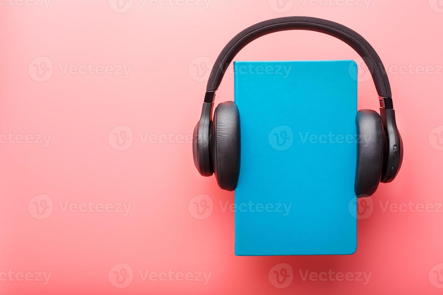 Headphones are worn on a book in a blue hardcover on a pink background, top view. photo