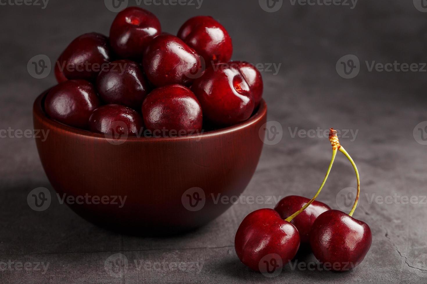 Ripe and juicy cherry berries on a black textural background in a brown cup, with water drops. Top view, close-up, Macro. photo