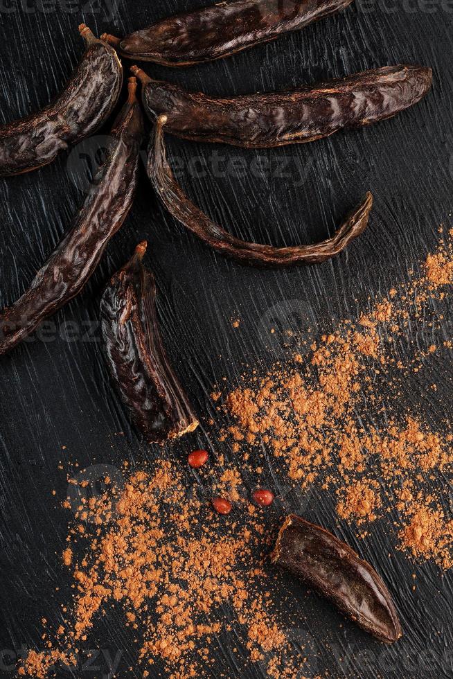 Carob carob fruit with powder on black background. Blast the Sweet powder from the pulp of the pods. photo