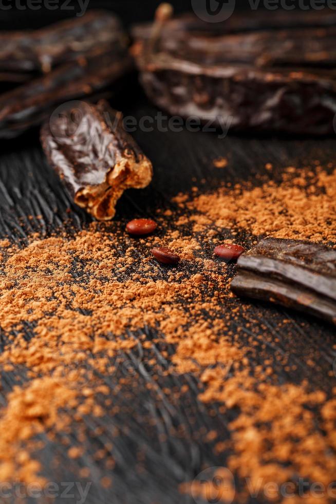 Carob carob fruit with powder on black background. Blast the Sweet powder from the pulp of the pods. photo