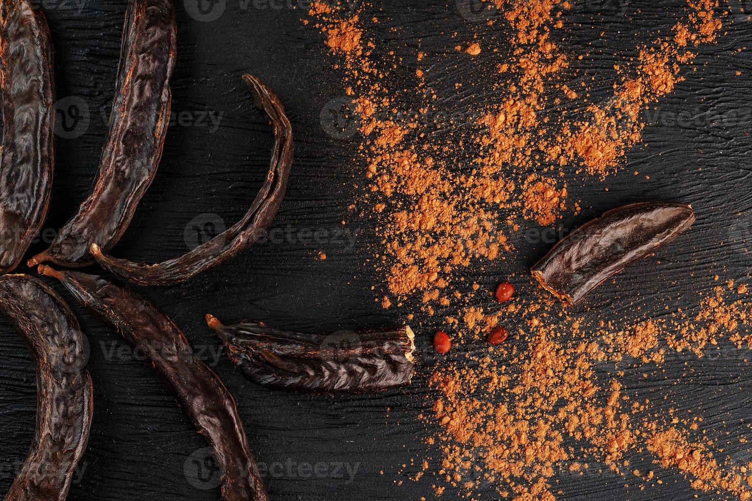 Carob carob fruit with powder on black background. Blast the Sweet powder from the pulp of the pods. photo