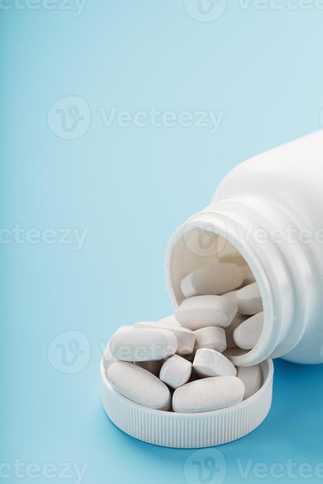 Vitamins and minerals in white capsules fell out of a white jar on a blue background. photo