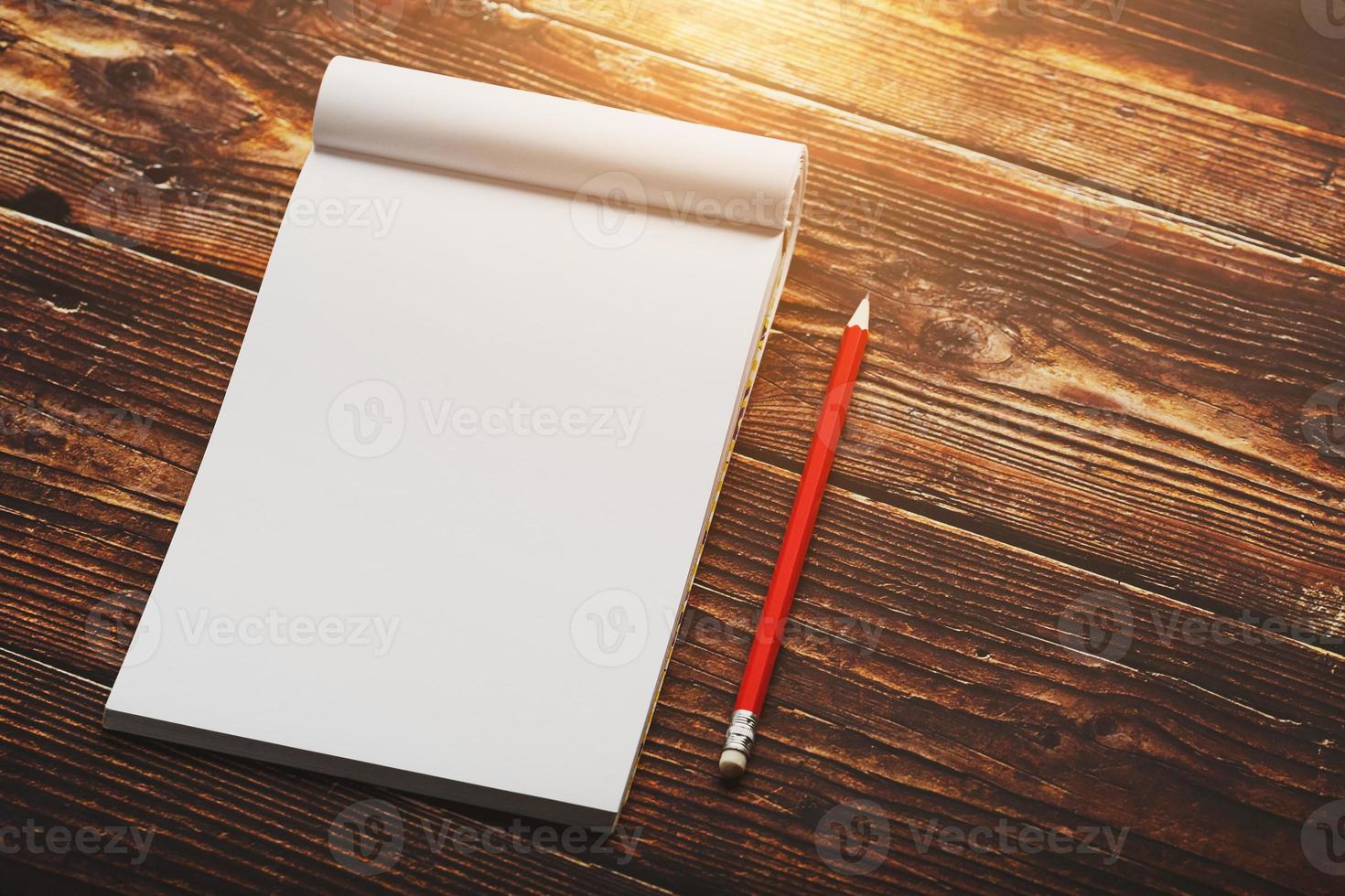 Notebook with a red pencil on a brown background with warm sunlight, for writing. Free empty space for writing on a blank sheet of a notebook. photo