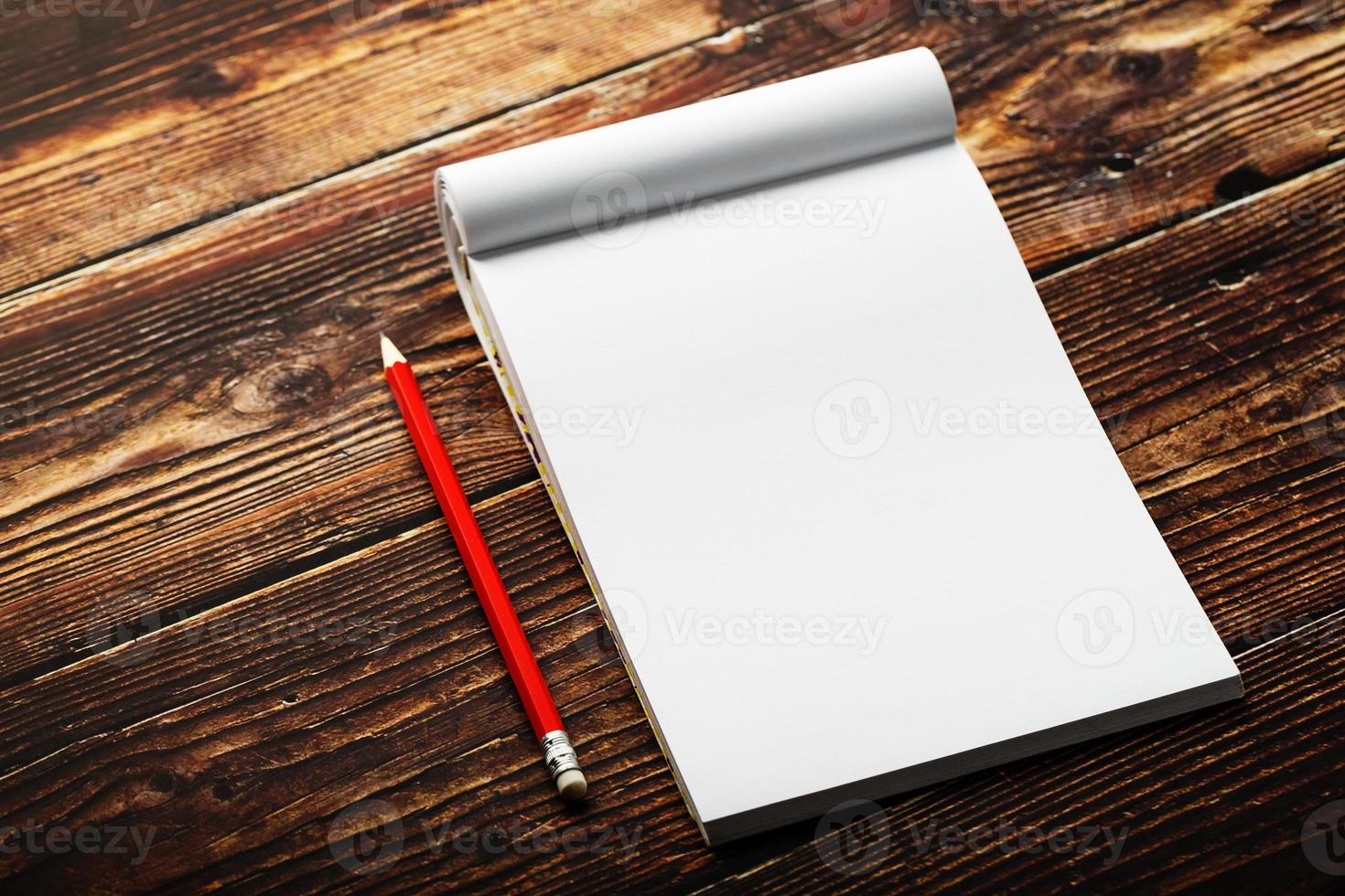 Notepad with red pencil on a brown wooden table background, for education, write goals and deeds photo