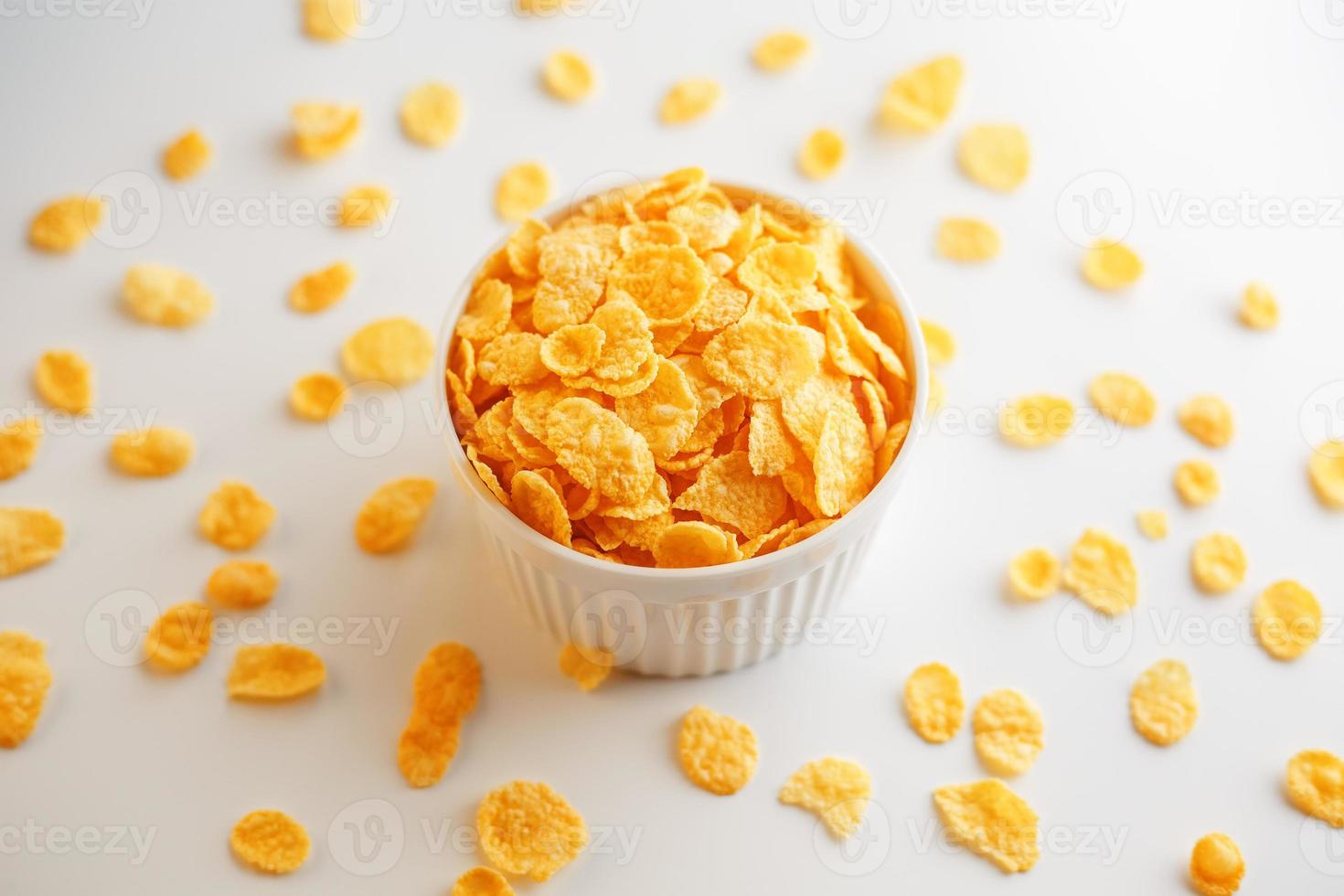 White cup with golden corn flakes, isolated on white background. Hopya crumbled around the cup. View from above photo