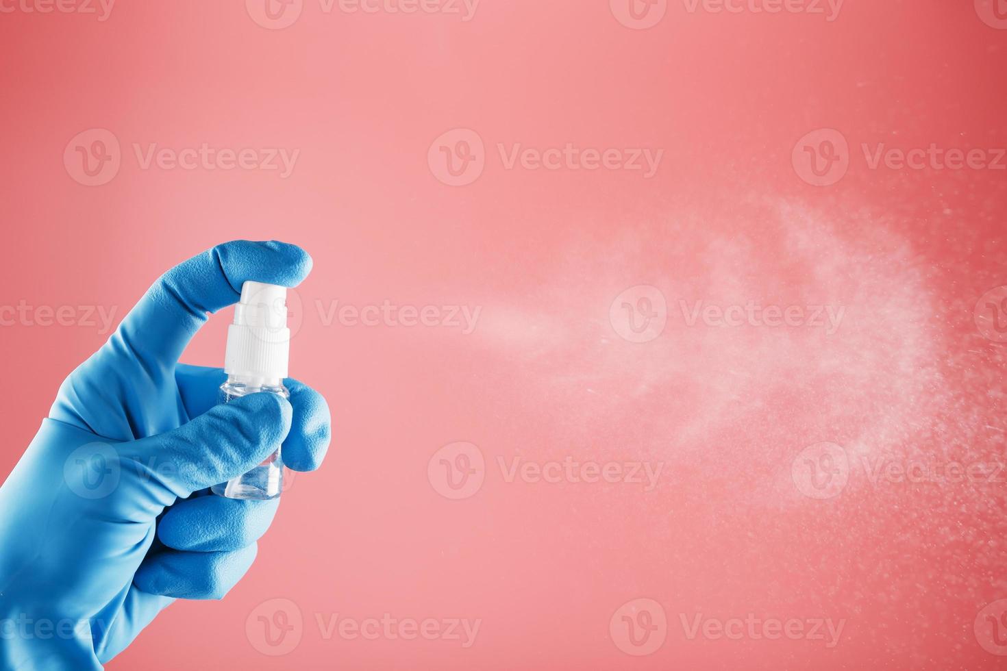 una mano con guantes azules sostiene un desinfectante sobre un fondo rosa. tratamiento antiséptico de manos a partir de desinfectante bacteriano. foto