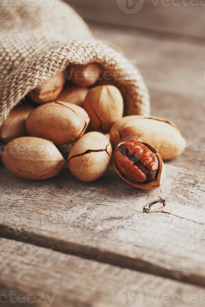 Pecans are spilled out of a burlap bag onto a wooden table in close-up. photo