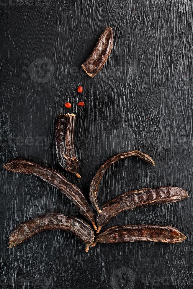 el fruto del algarrobo sobre fondo negro texturizado en forma foto