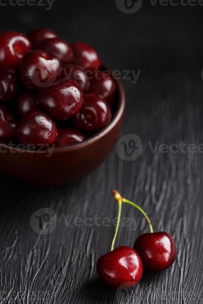 Ripe and juicy cherry berries on a black textural background in a brown cup, with water drops. Top view, close-up. photo
