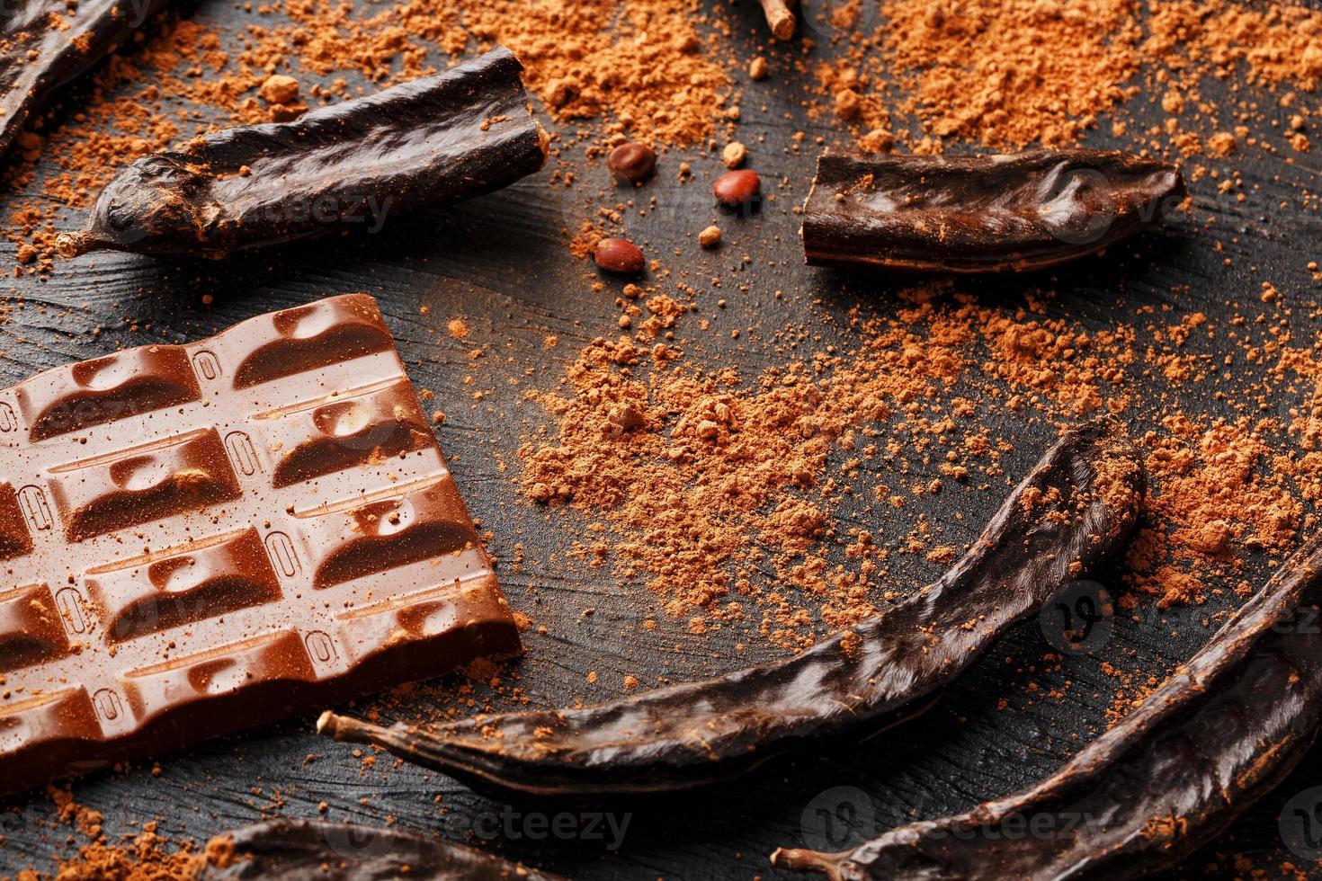 Carob chocolate and carob fruit powder on dark background. A tasty and useful substitute for chocolate. Health benefits. Soft contrast photo