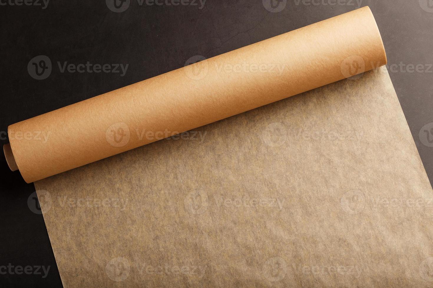 A roll of unfolded brown parchment paper, for baking food in on a dark background, top view. photo