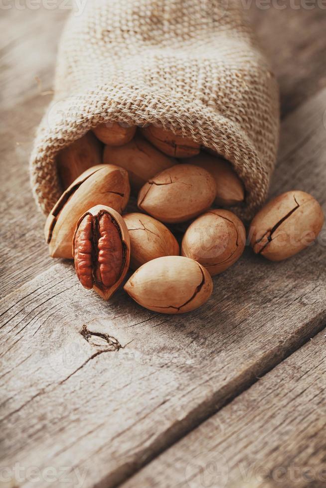 Pecans are spilled out of a burlap bag onto a wooden table in close-up. photo