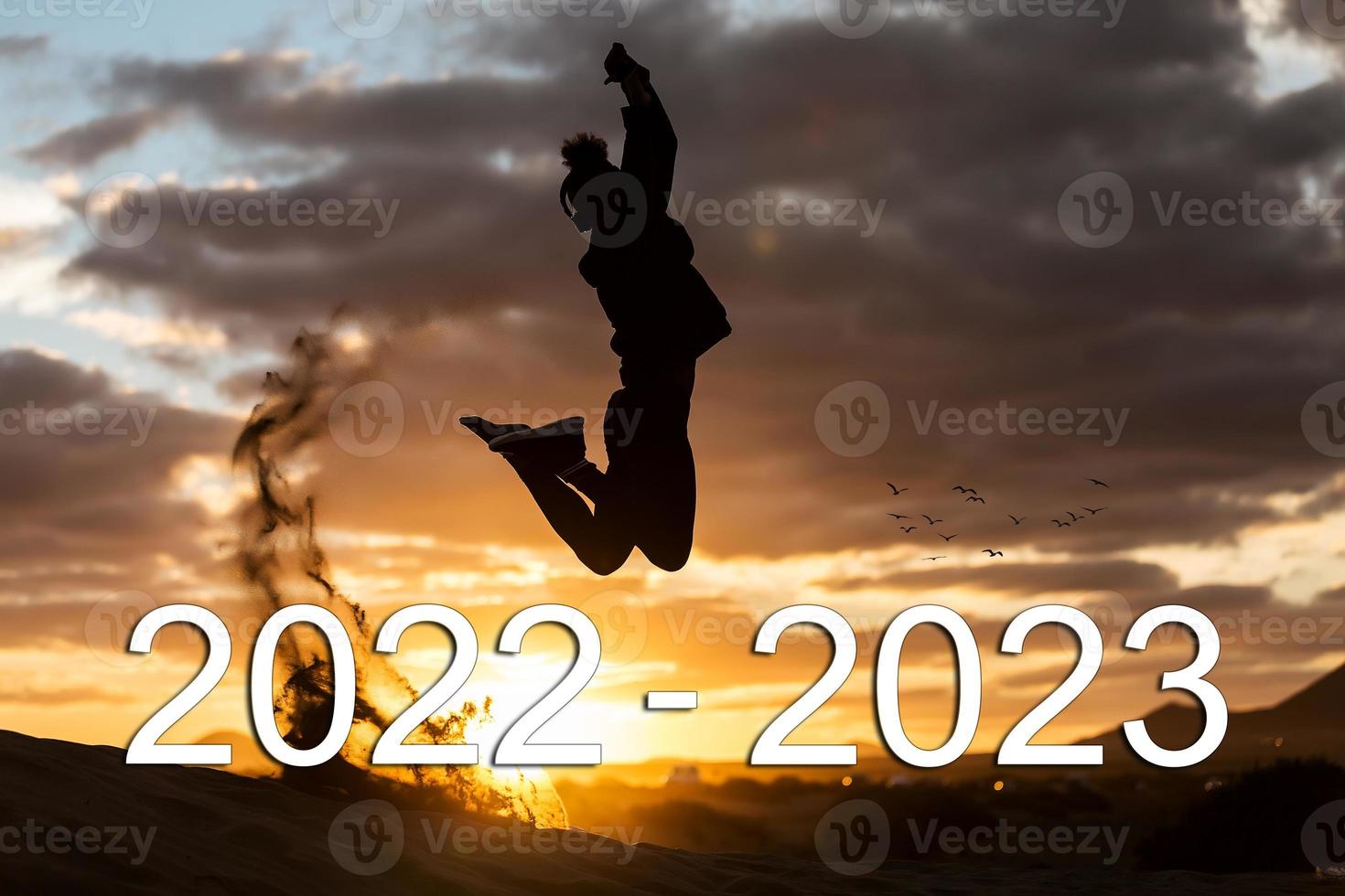 silhouette of man jumping from year 2022 to 2023 with arms up at sunset with birds in background, year change concept. photo